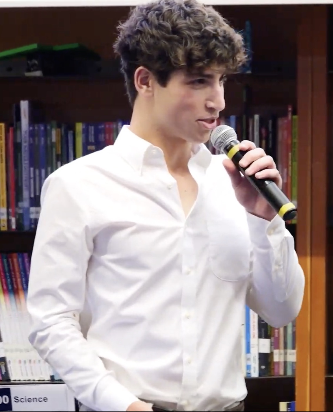 Charles Greenwald speaking into a microphone in a white button-down shirt